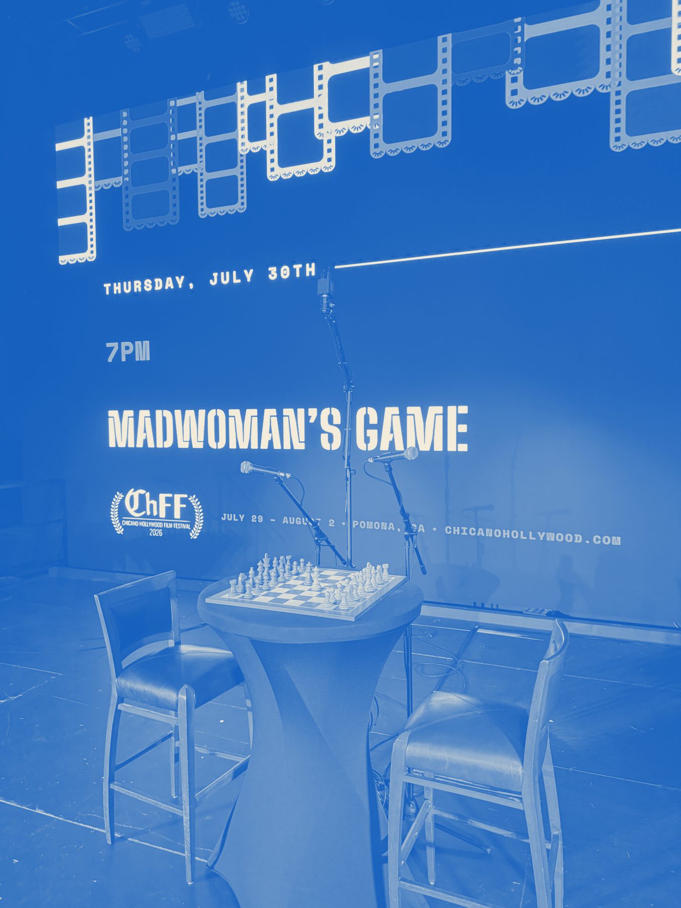 The chess match staged — board, mics and chairs under the projected title card